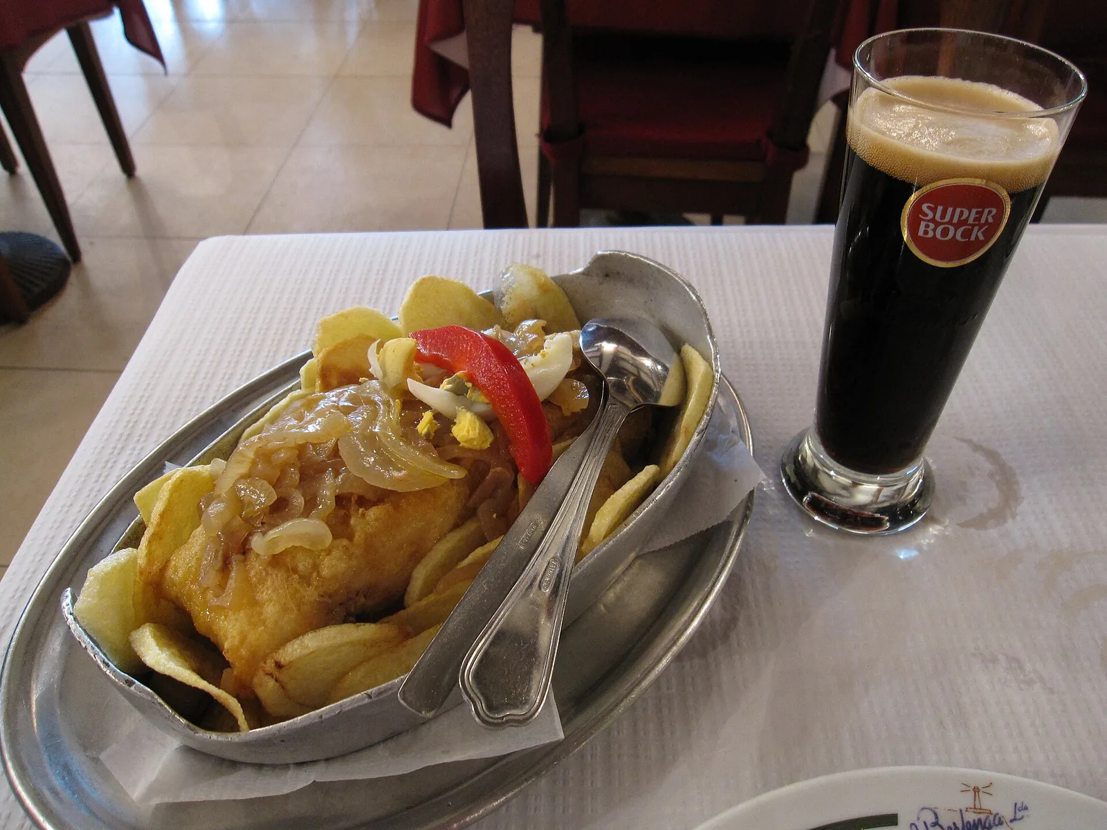 Boat-shaped dish of fish with potato chips, onions and peppers
