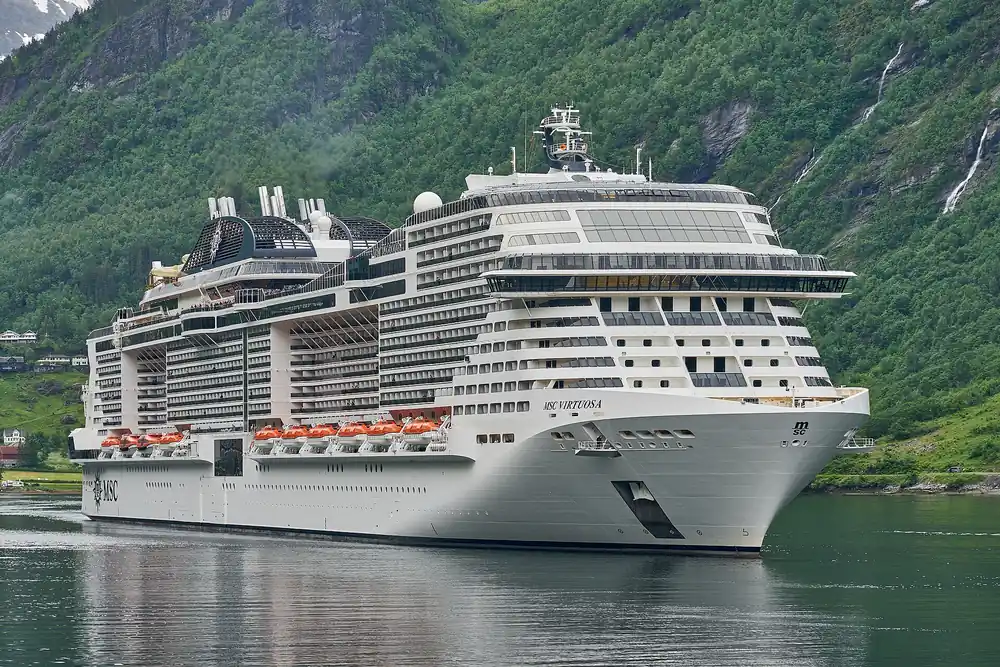 Cruise ship MSC Virtuosa in Geirangerfjord beneath steep forested cliffs