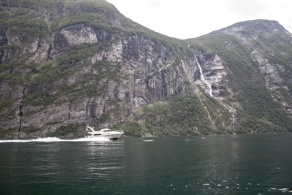 White motor yacht cruising a narrow Norwegian fjord below green cliffs
